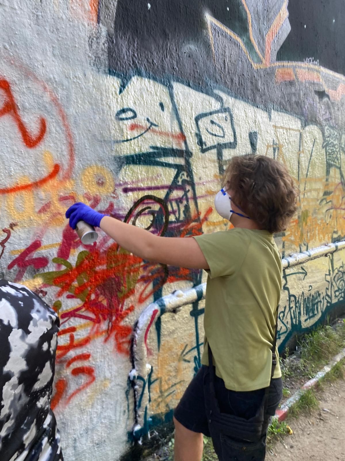Jugendlicher mit Schutzmaske und Handschuh gestaltet eine Graffitiwand