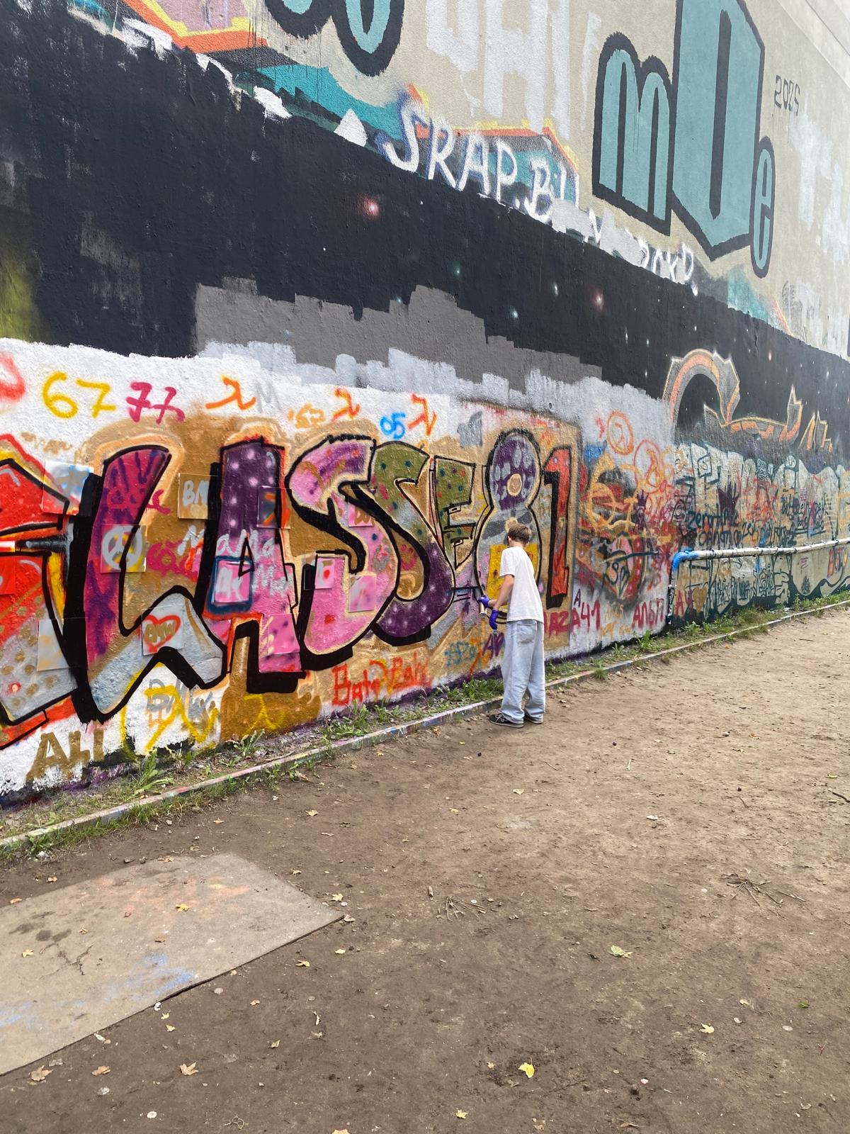 Jugendlicher arbeitet an einer großflächigen Graffitiwand