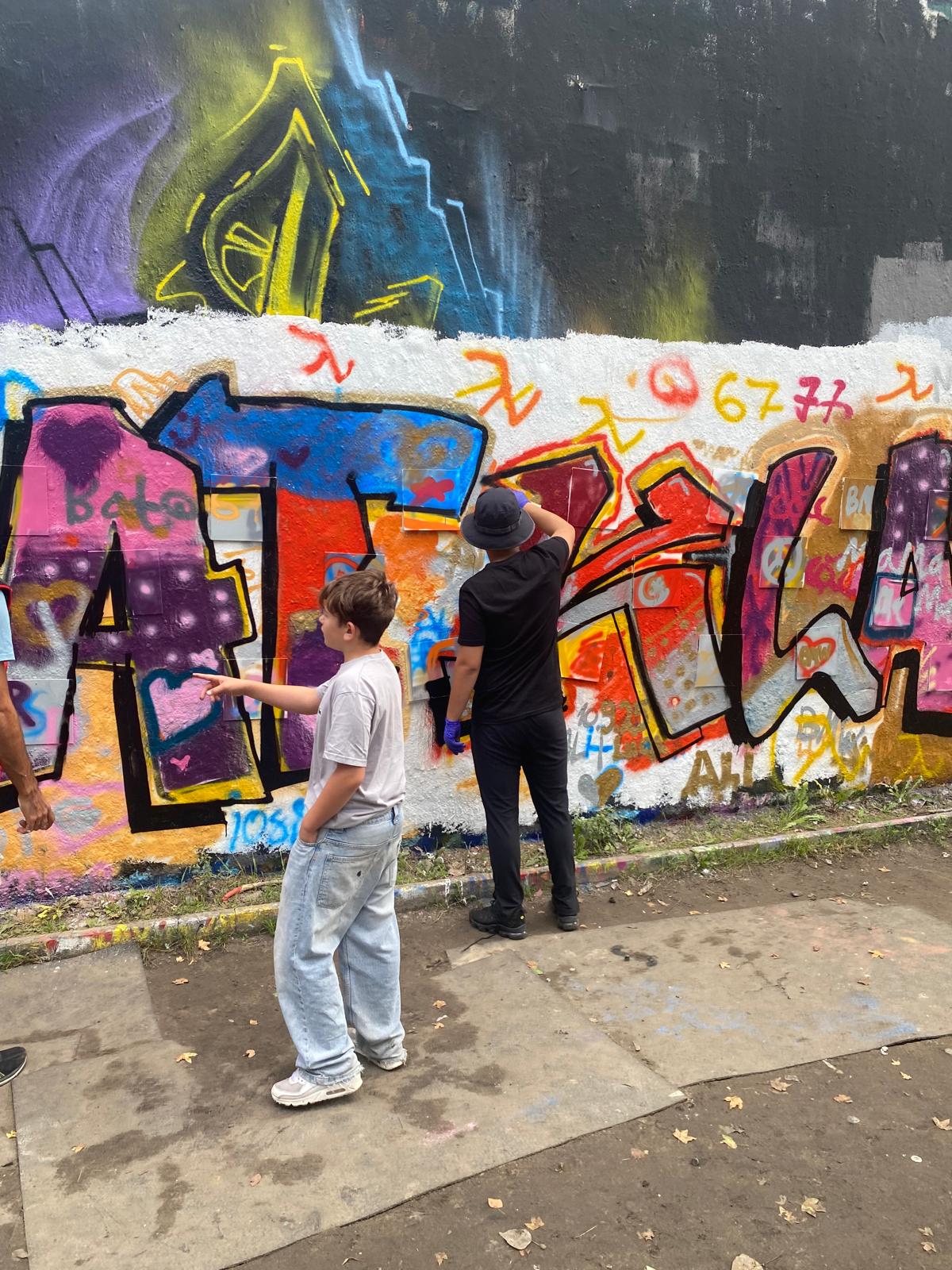 Jugendliche gestalten gemeinsam eine farbige Graffitiwand