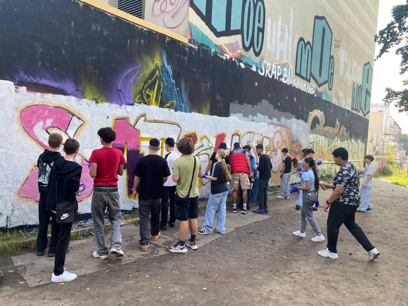 Gruppe von Jugendlichen arbeitet gemeinsam an einer Graffitiwand
